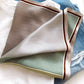 Striped small mulberry silk square scarf with brown and green lines folded on a white t-shirt and denim background