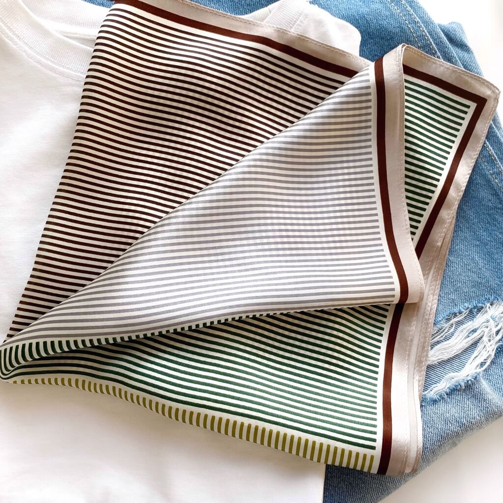 Striped small mulberry silk square scarf with brown and green lines folded on a white t-shirt and denim background