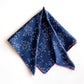 Folded River Minami square mulberry silk scarf in navy blue with white geometric prints and red trim.
