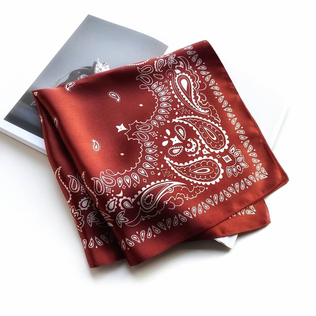folded brick red mulberry silk square scarf with white paisley pattern on a white background