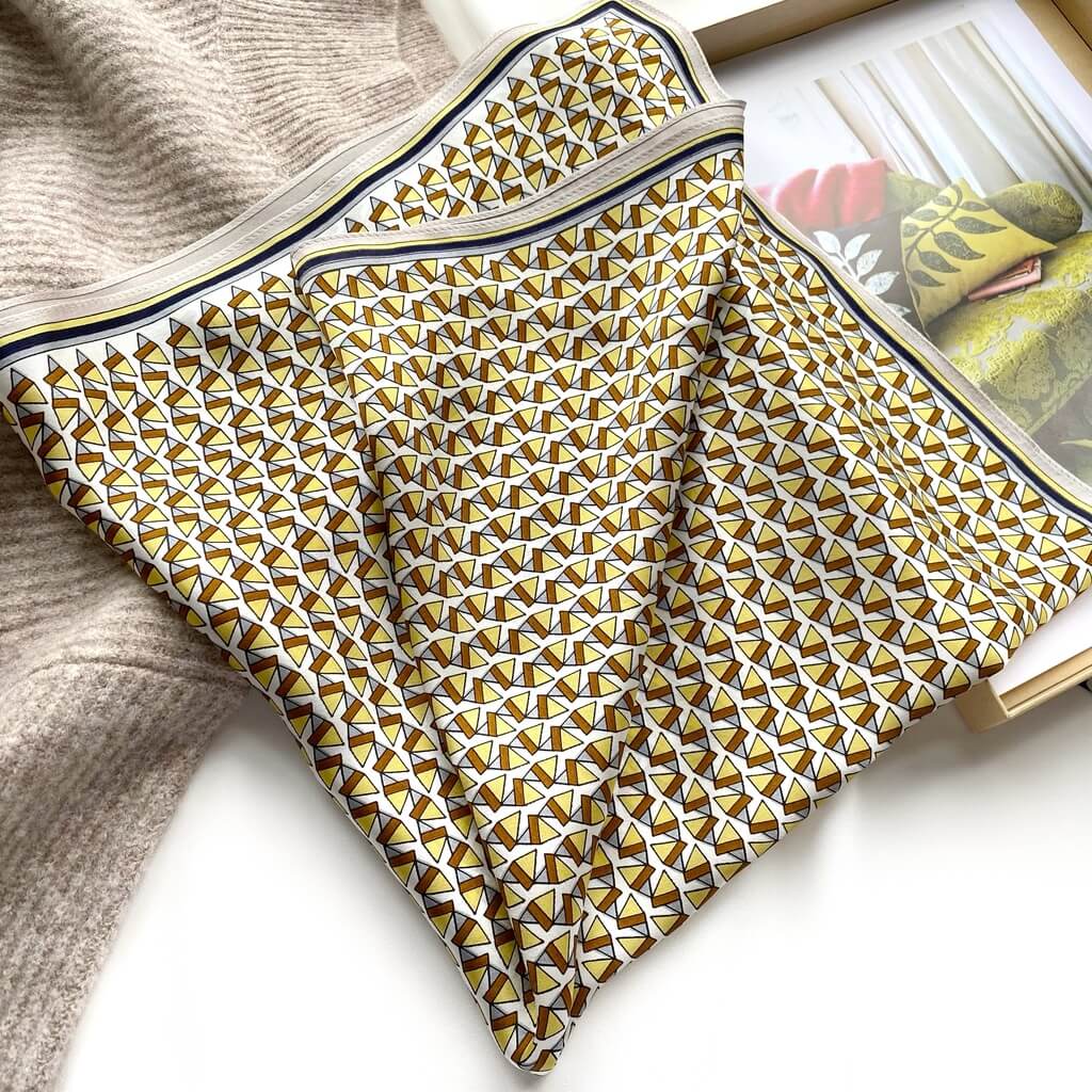 Folded yellow brown mulberry silk square scarf with geometric pattern on a magazine