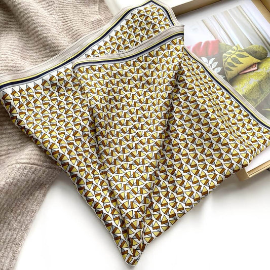 Folded yellow brown mulberry silk square scarf with geometric pattern on a magazine