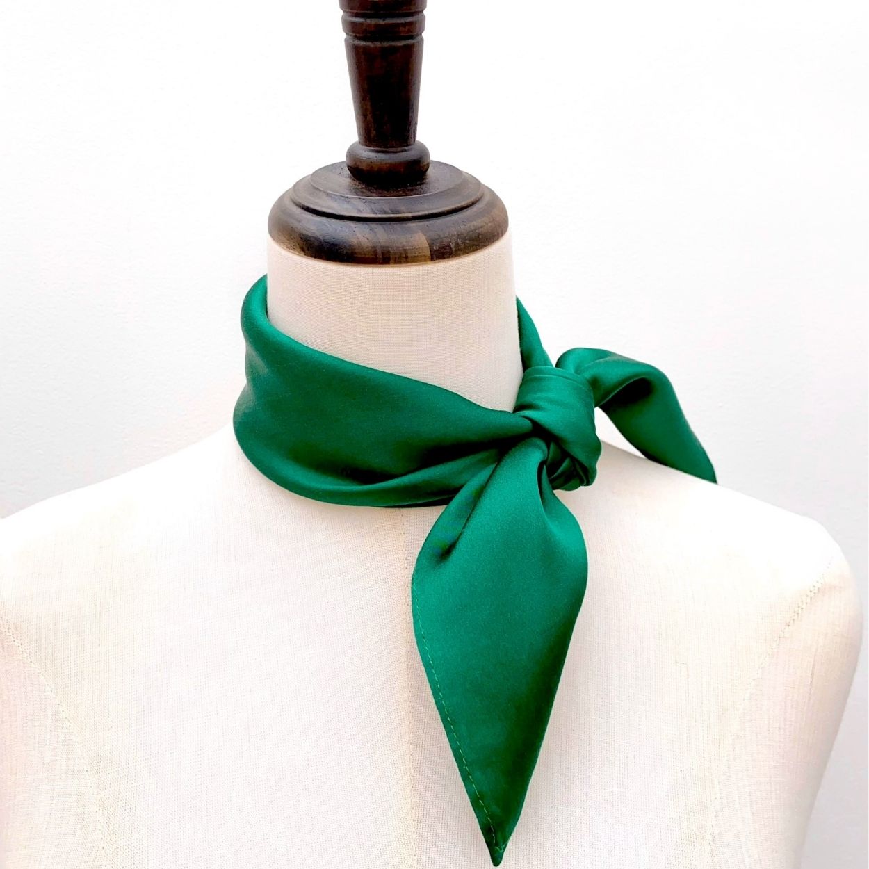 A forest green mulberry silk square scarf tied in a knot on mannequin neck, set against a plain white background.