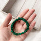 Green silk hair tie held in a hand on a light wooden surface