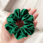 Green silk satin scrunchie held in a hand with a light wooden surface in the background