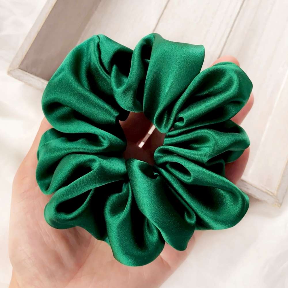 Large green mulberry silk scrunchie held in a hand with a light wooden background