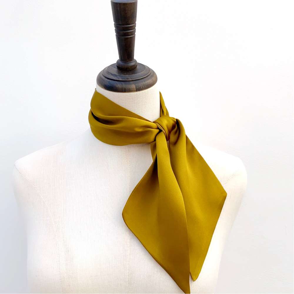 golden olive coloured silk scarf tied around a mannequin neck on a white background