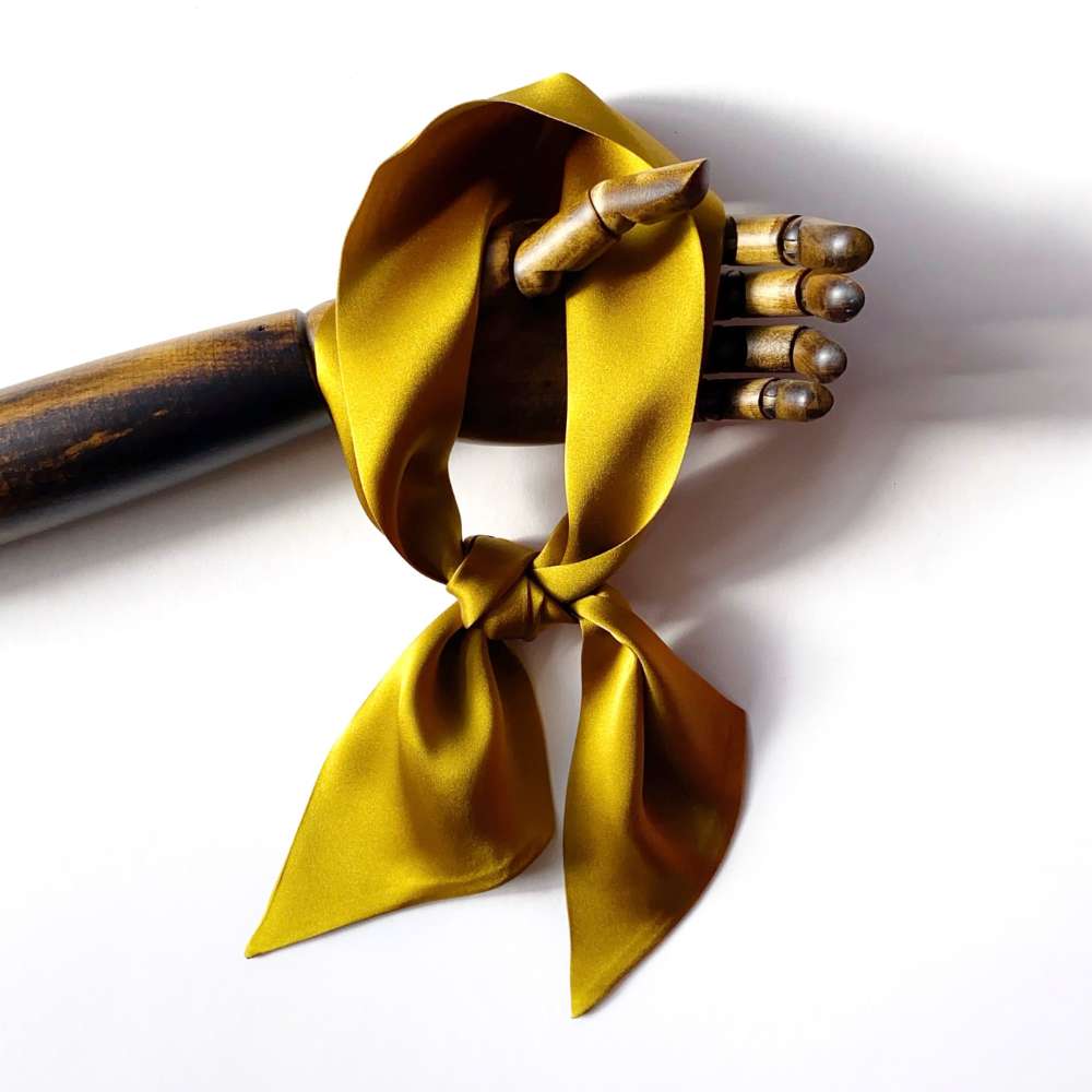 wooden hand hold a golden olive coloured silk scarf on a white background