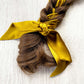 Braided hair with a golden olive coloured skinny scarf on a textured white background
