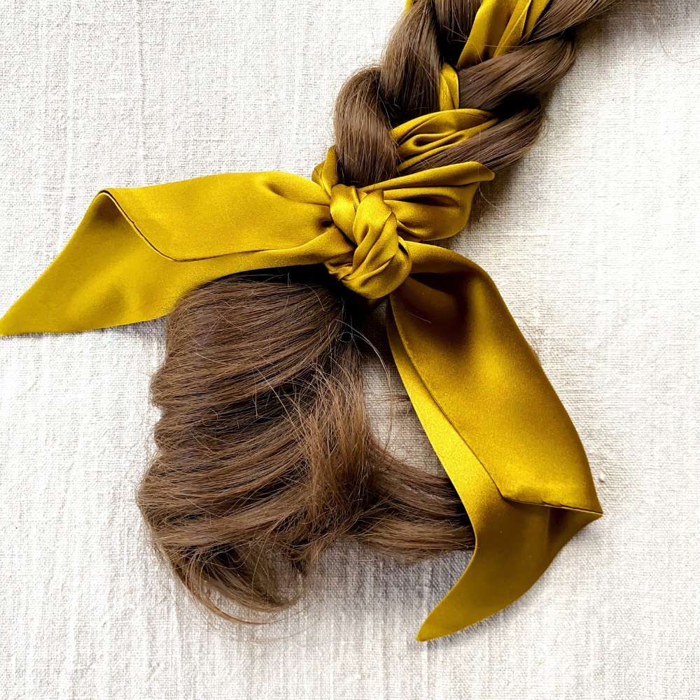 Braided hair with a golden olive coloured skinny scarf on a textured white background