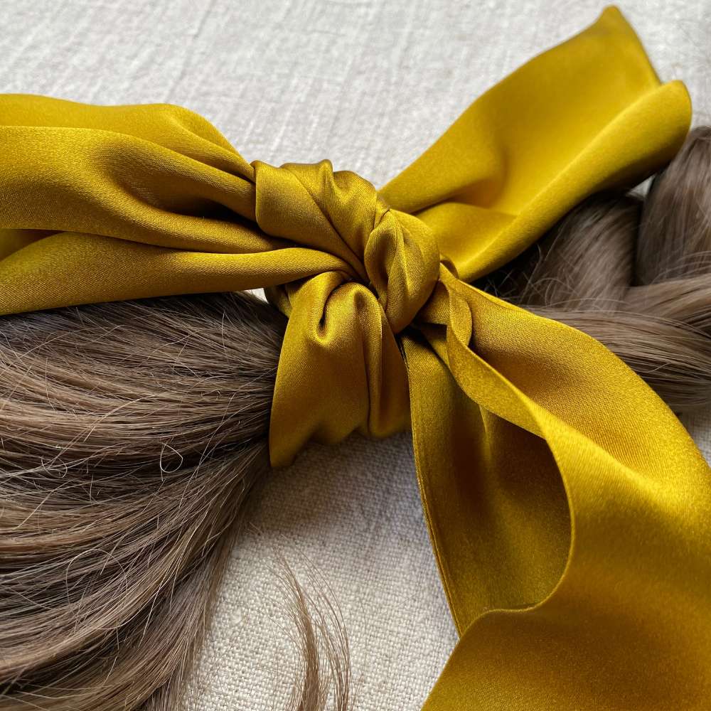 golden olive coloured silk hair bow on a person's hair against a neutral background