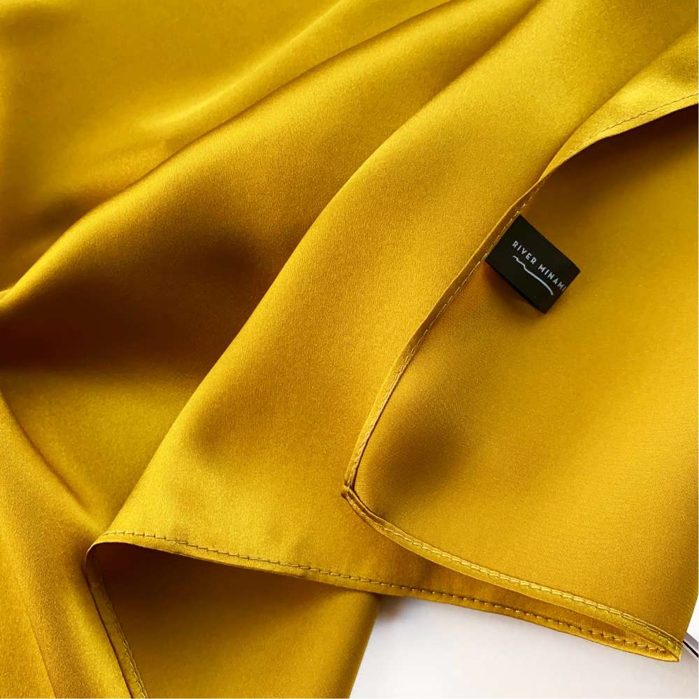 Close-up of a golden olive mulberry silk scarf with a brand label on a white background