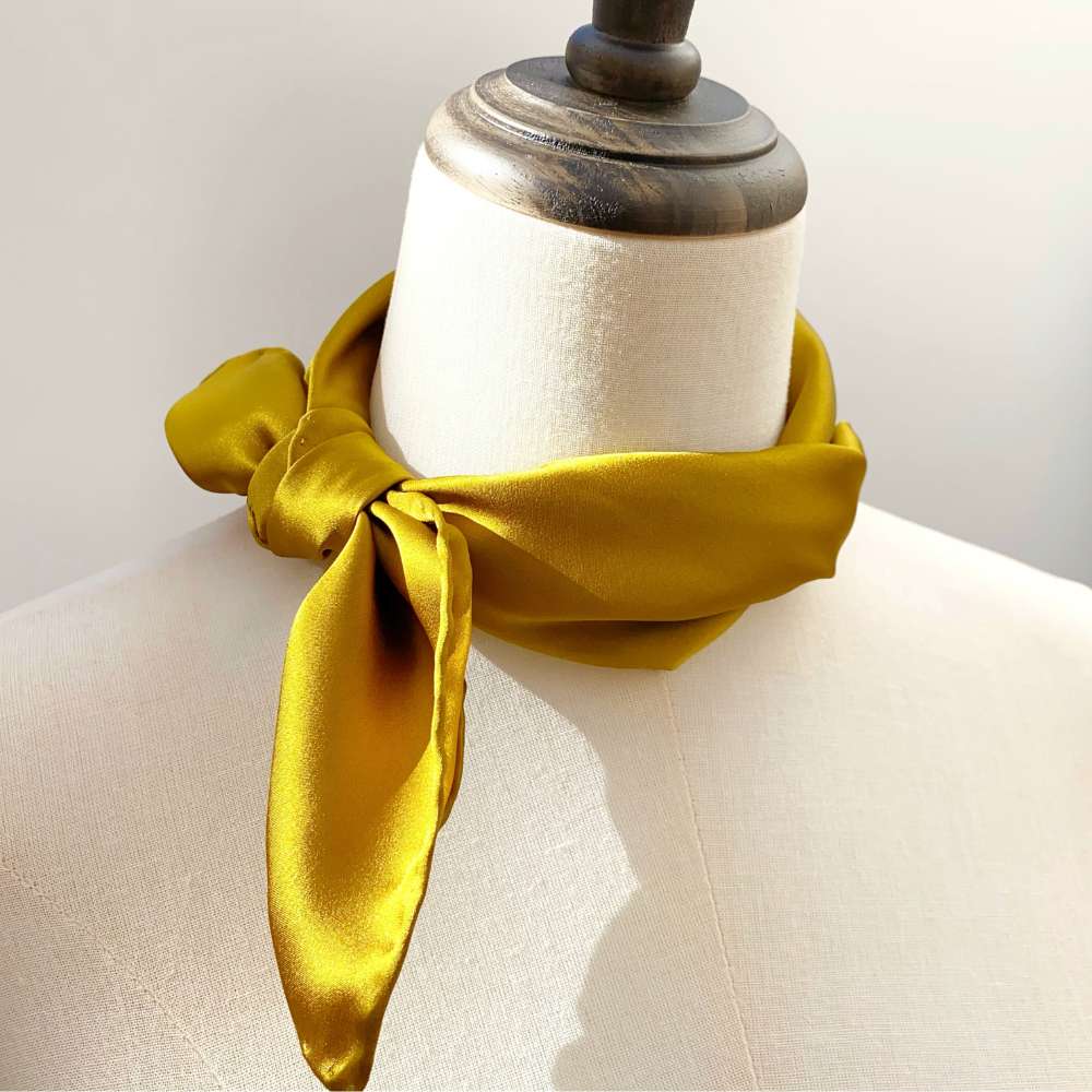 Yellow silk bandana scarf draped around a mannequin neck against a neutral background