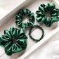 Set of green mulberry silk satin scrunchies and hair ties on a light wooden surface