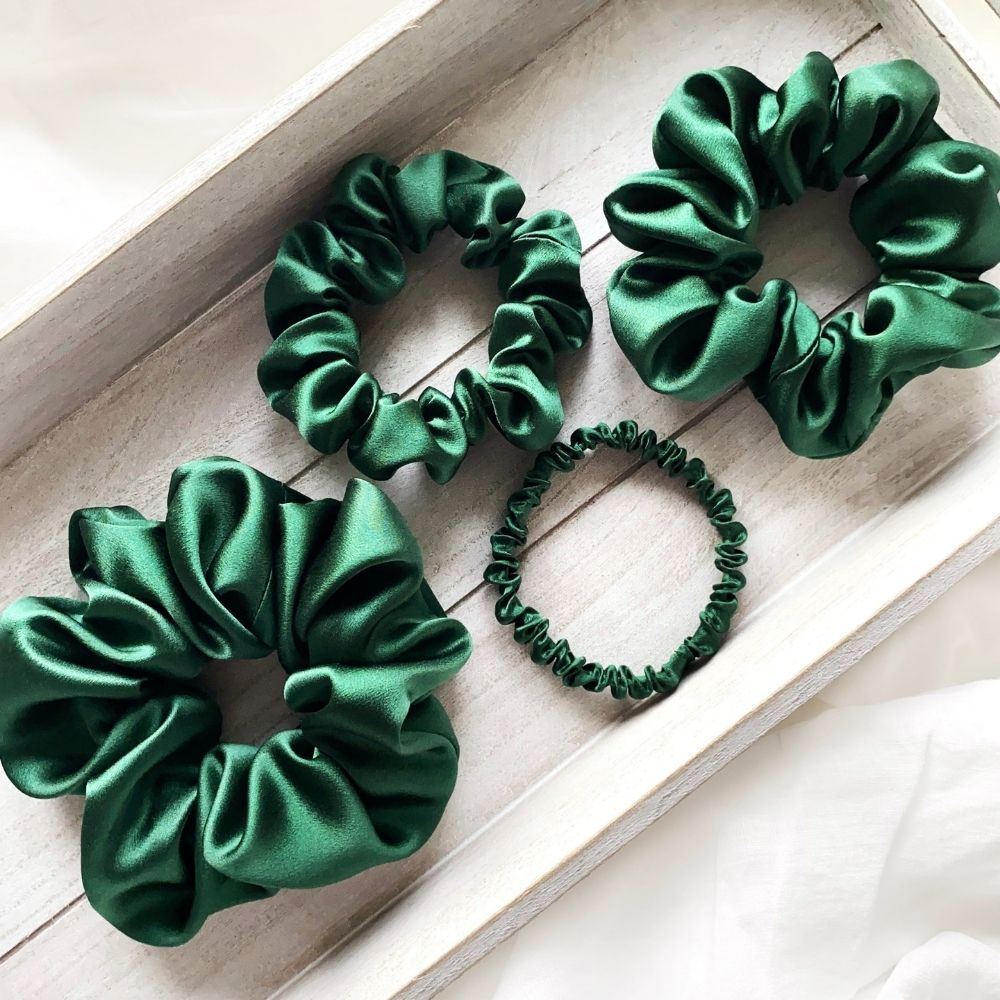Set of green mulberry silk satin scrunchies and hair ties on a light wooden surface
