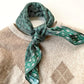 green paisley print mulberry silk twill bandana neck scarf placed on a cream colour crew neck jumper