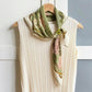 Floral scarf draped over a white garment on a wooden hanger against a light background