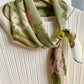 Green floral scarf with a scarf clip on a cream top.