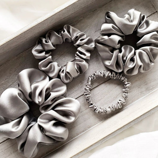Four gray mulberry silk satin scrunchies and silk hair ties on a wooden surface
