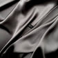 Close-up of slate grey mulberry silk satin fabric showing smooth texture and River Minami washing label.