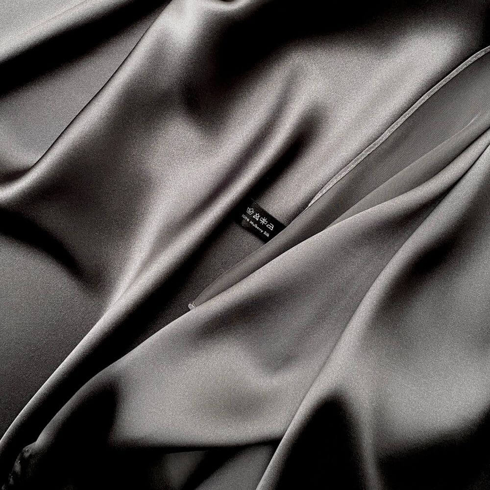 Close-up of slate grey mulberry silk satin fabric showing smooth texture and River Minami washing label.
