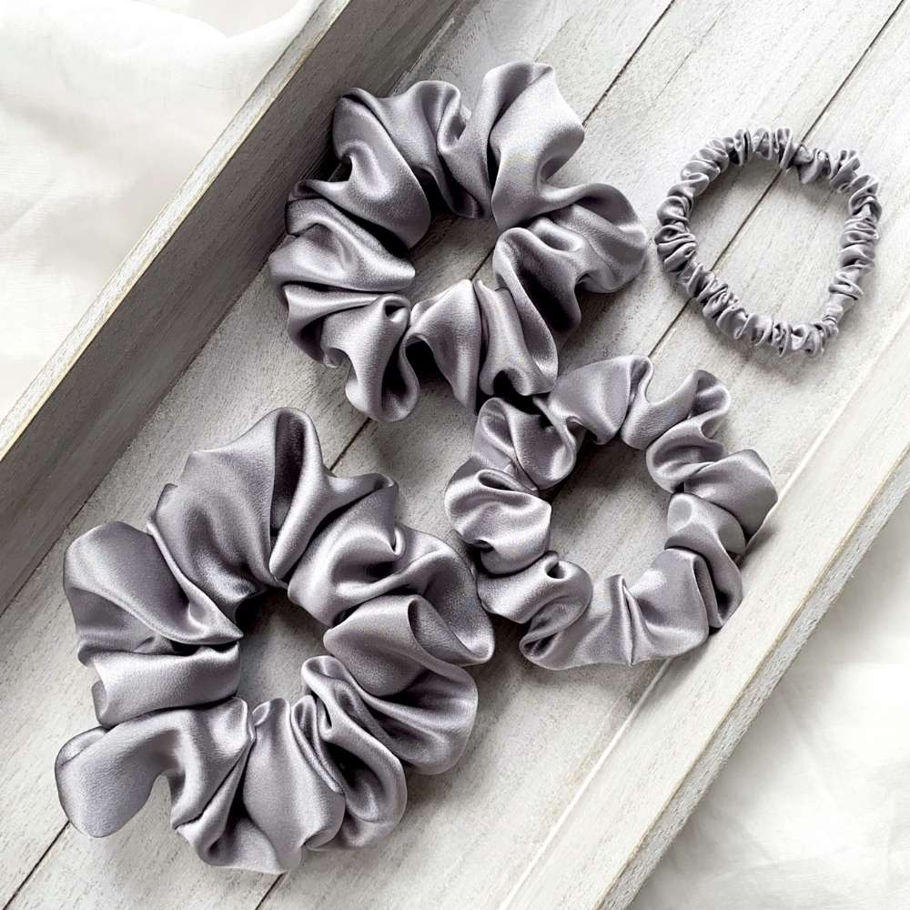 Set of gray mulberry silk satin scrunchies on a light wooden surface