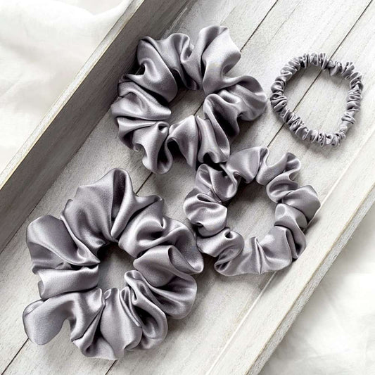 Set of gray mulberry silk satin scrunchies on a light wooden surface
