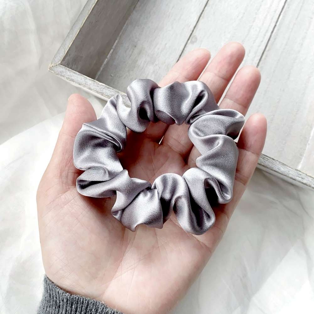 grey mulberry silk satin scrunchie held in a hand with a light background