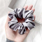 Hand holding a gray mulberry silk satin scrunchie against a light background