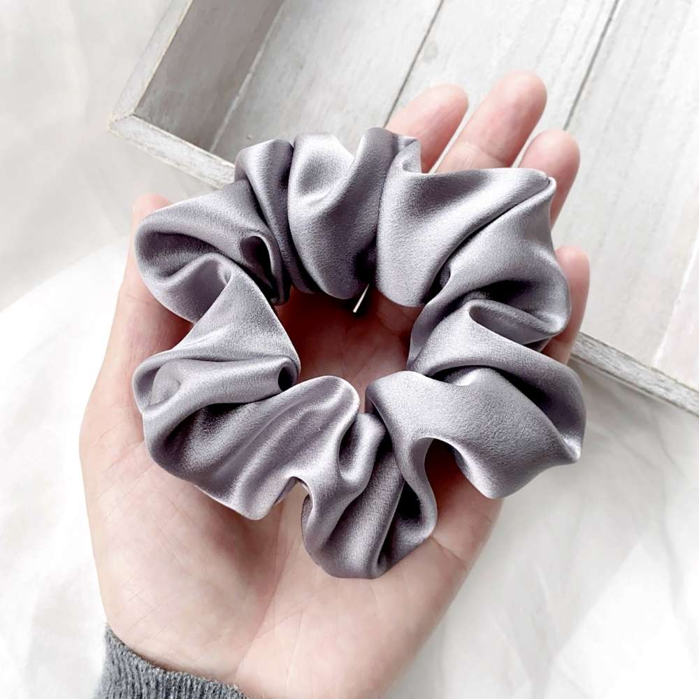 Hand holding a gray mulberry silk satin scrunchie against a light background