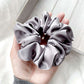 Gray mulberry silk satin scrunchie held in a hand against a neutral background