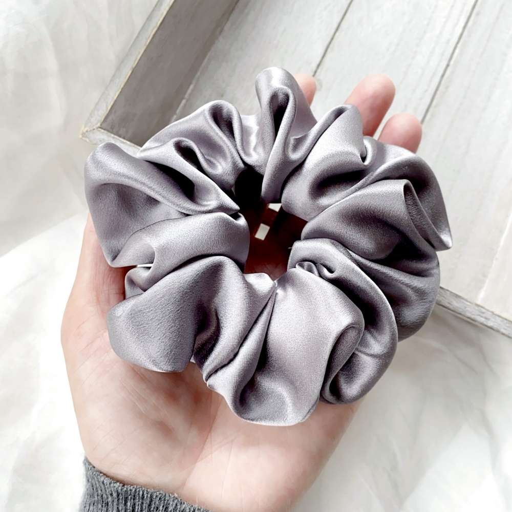 Gray mulberry silk satin scrunchie held in a hand against a neutral background