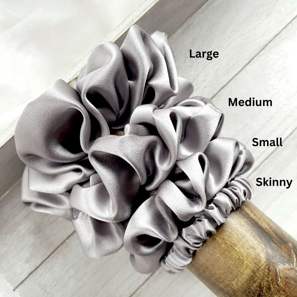 Set of grey mulberry silk satin scrunchies labeled 'Large', 'Medium', 'Small', and 'Skinny' on a wooden surface.