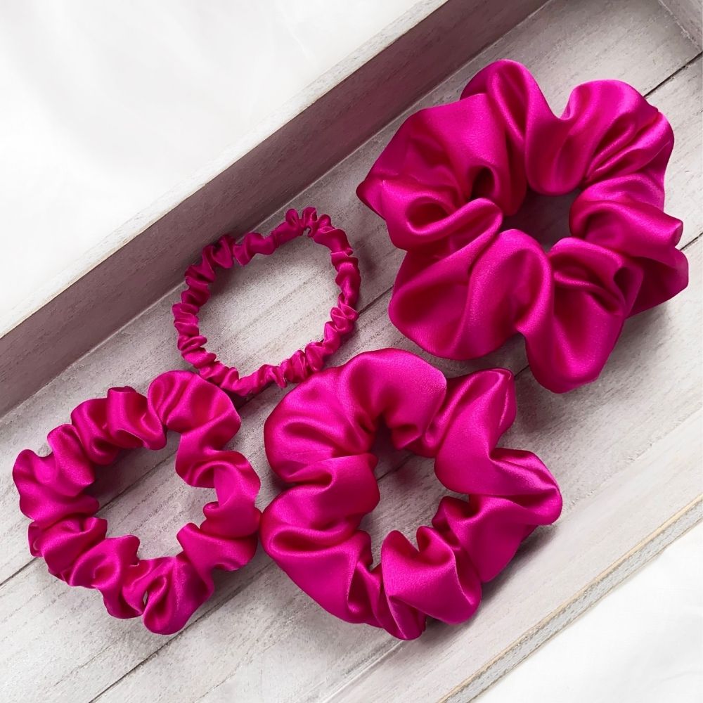 set of hot pink pure mulberry silk satin scrunchies and hair ties on a wooden surface.