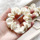 ivory cream mulberry silk satin scrunchie held in a hand with a blurred background