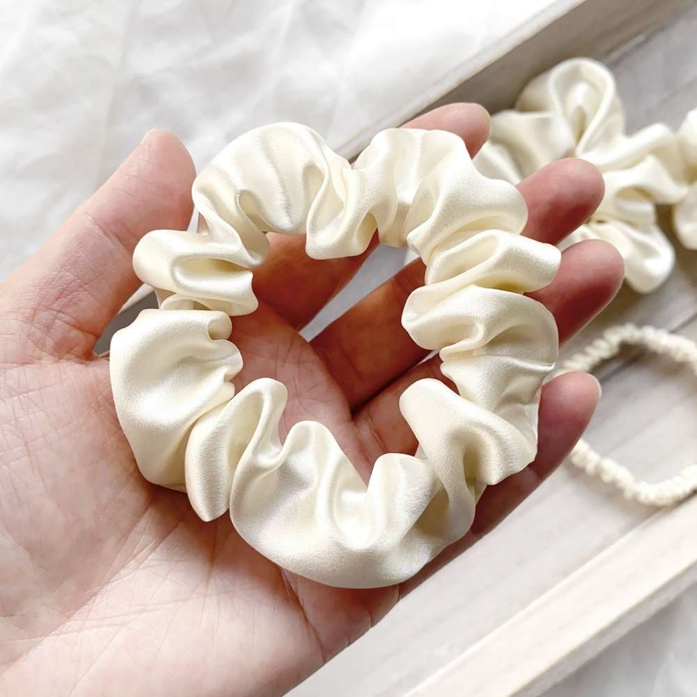 ivory cream mulberry silk satin scrunchie held in a hand with a blurred background