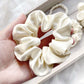 ivory cream mulberry silk satin scrunchie held in a hand with more scrunchies in the background.