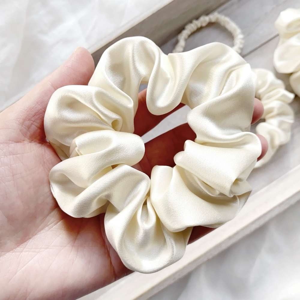 ivory cream mulberry silk satin scrunchie held in a hand with more scrunchies in the background.