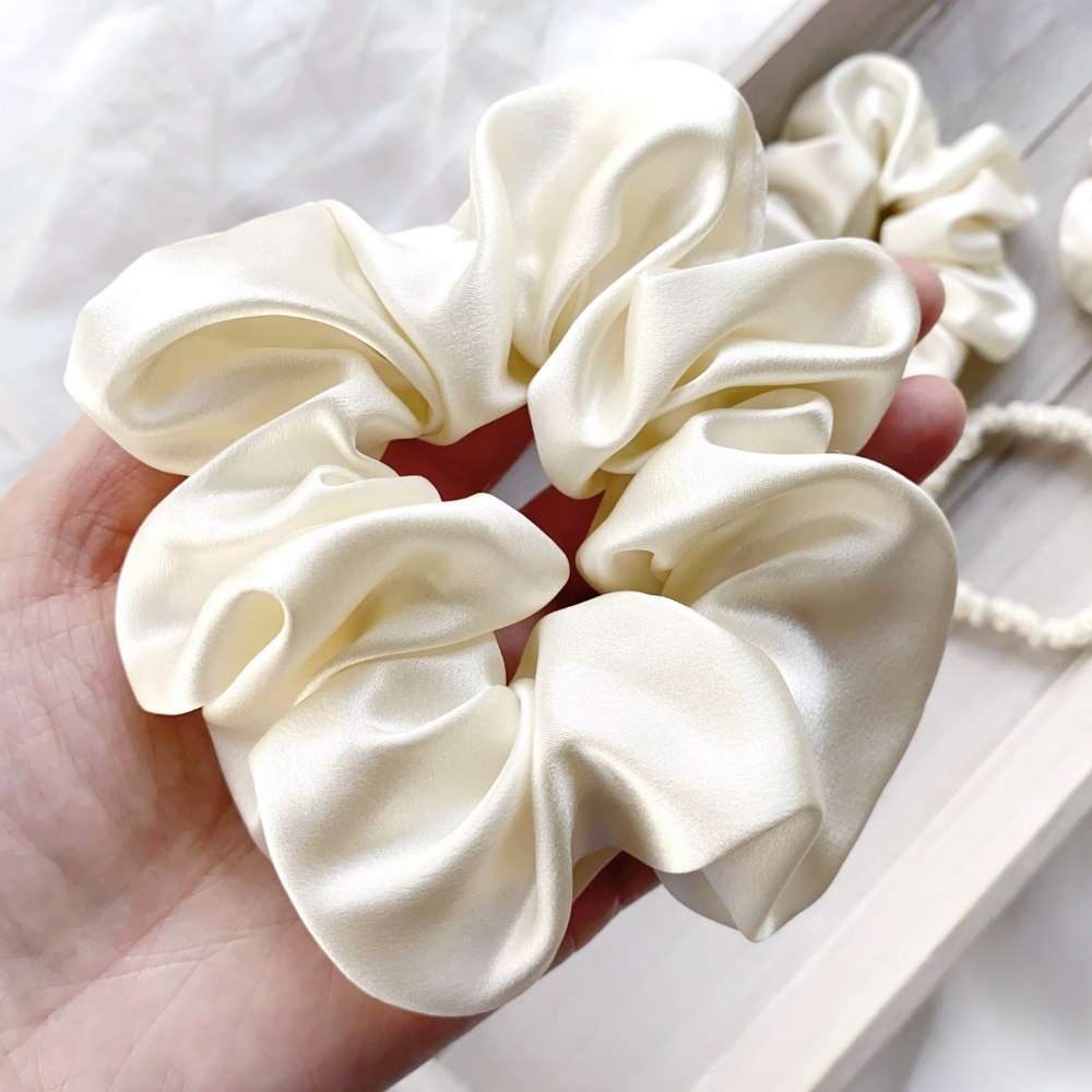 large ivory cream mulberry silk satin scrunchie held in a hand with a white background