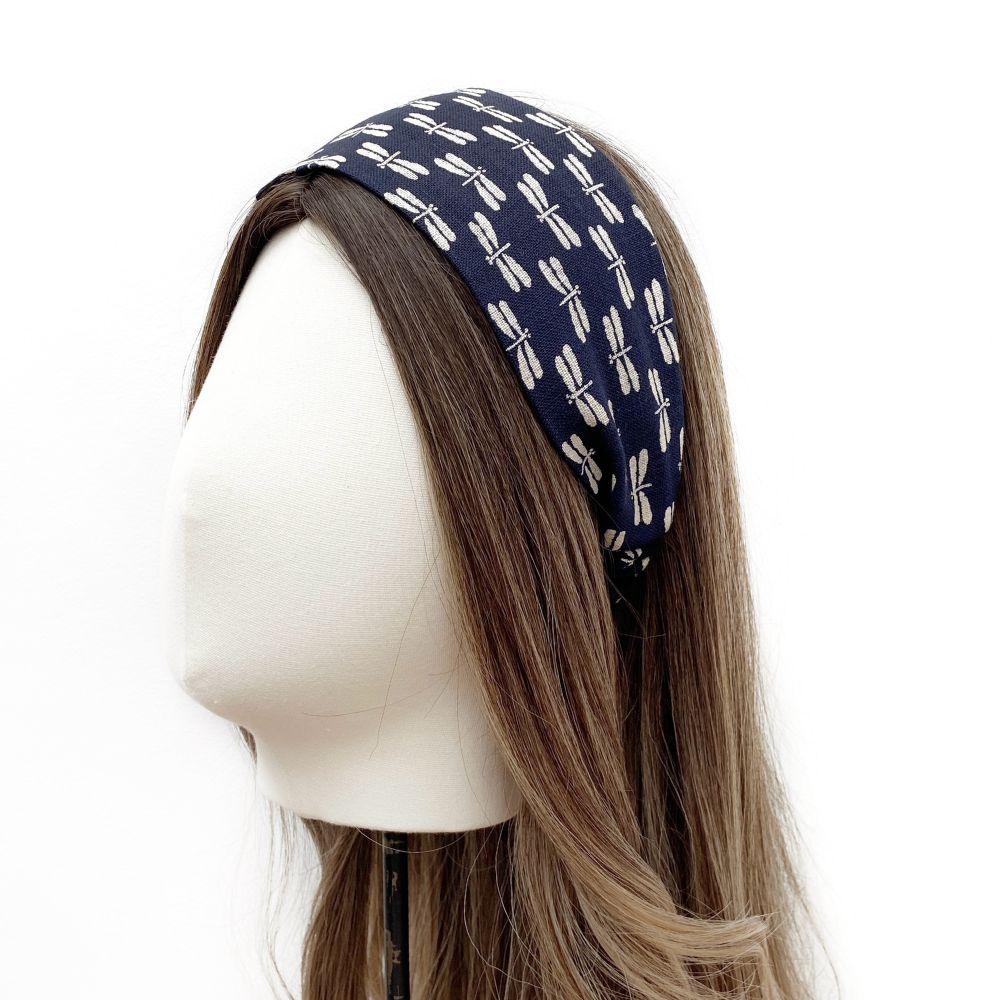 A navy blue cotton fabric headband with a white dragonfly pattern, displayed on a brown mannequin head.