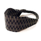 A wide cotton fabric headband with an elastic back, featuring a repeating arrow pattern in beige and black.