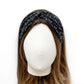 A black twisted headband with a white dragonfly pattern, displayed on a white mannequin head with brown hair against a white background.