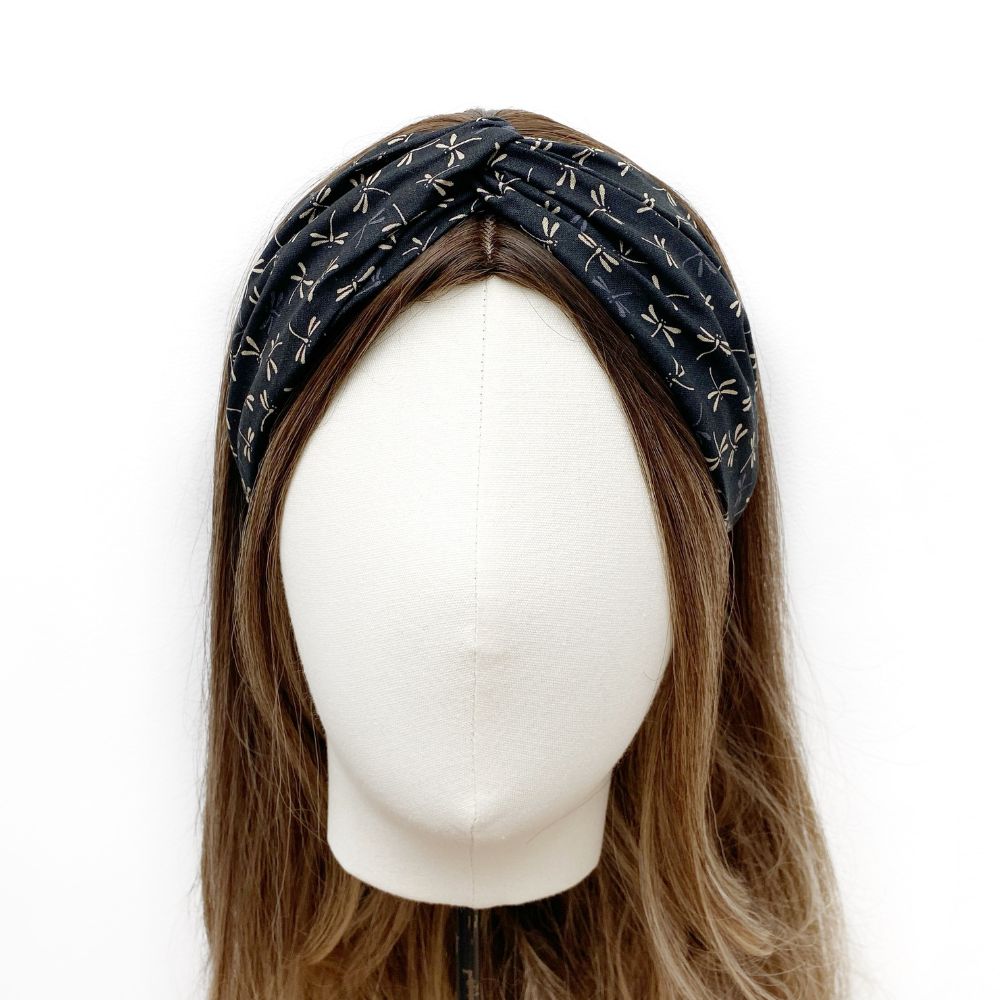 A black twisted headband with a white dragonfly pattern, displayed on a white mannequin head with brown hair against a white background.