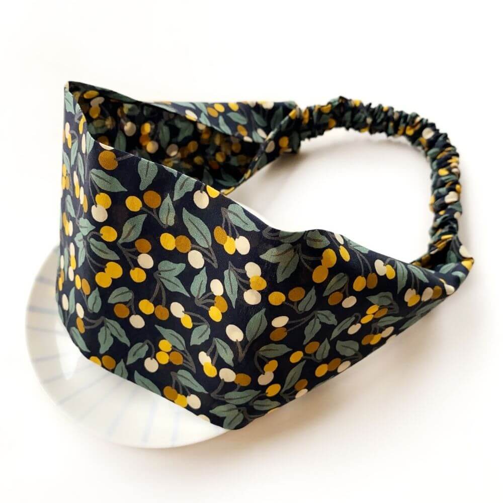 Liberty Cherry Drop cotton headband with wide flat front and elasticated back, shown in a curved angled view.
