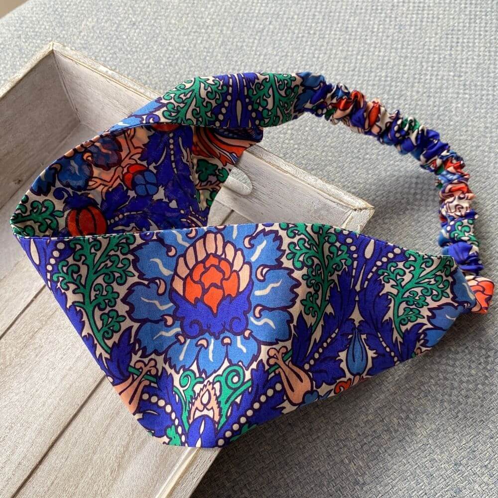 Liberty Electric Nouveau print cotton headband with a wide flat band and elasticated back, showing its bold blue, orange and green ornamental pattern.