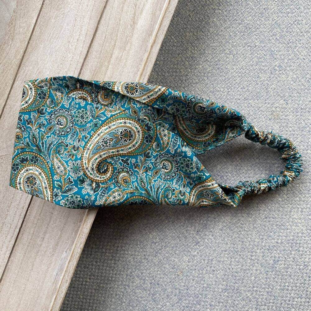 Liberty Lee Manor paisley print cotton headband displayed diagonally on a wooden surface, showing the full width of the patterned band.