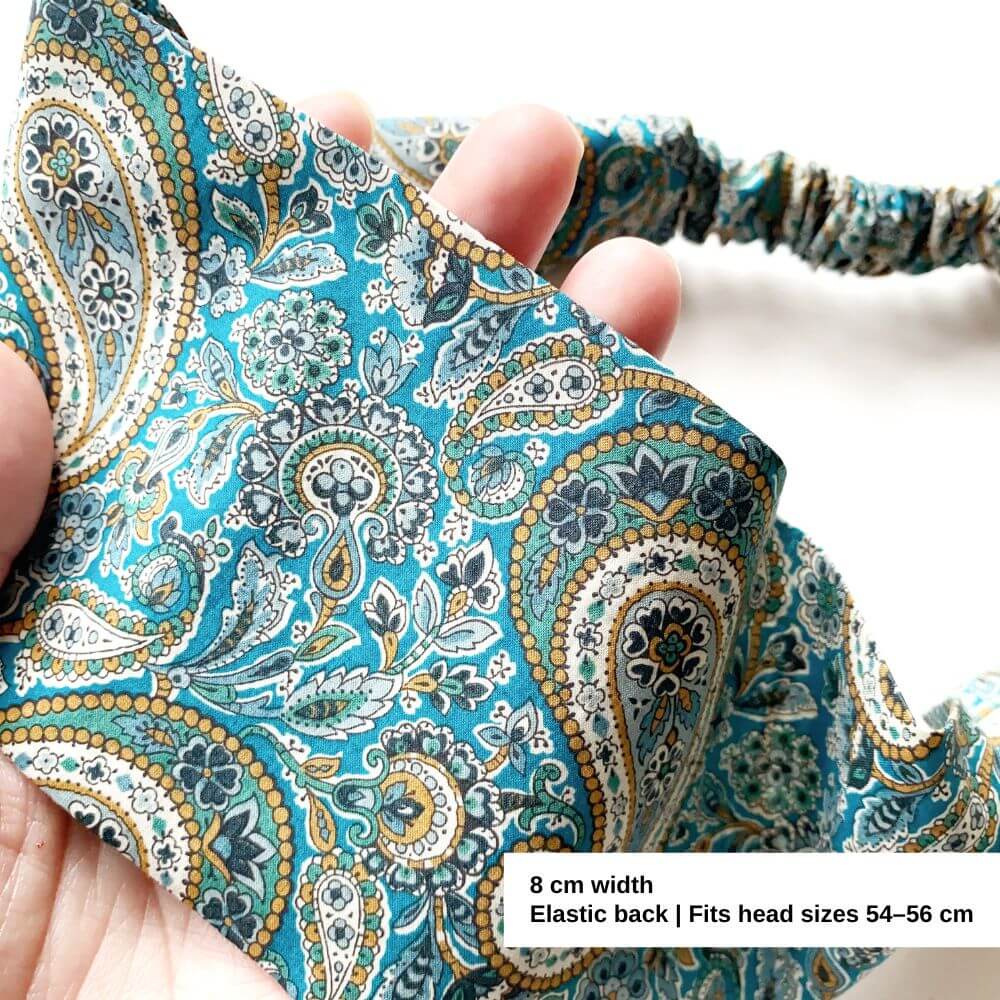 Paisley patterned headband held by a hand with product details.