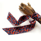 A navy blue liberty london silk twilly scarf with a red and orange floral pattern, styled on a wooden mannequin hand against a white background.