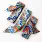 liberty silk skinny neck scarf with traditional japanese motifs in blue, orange, green, and white, arranged on a plain white background.