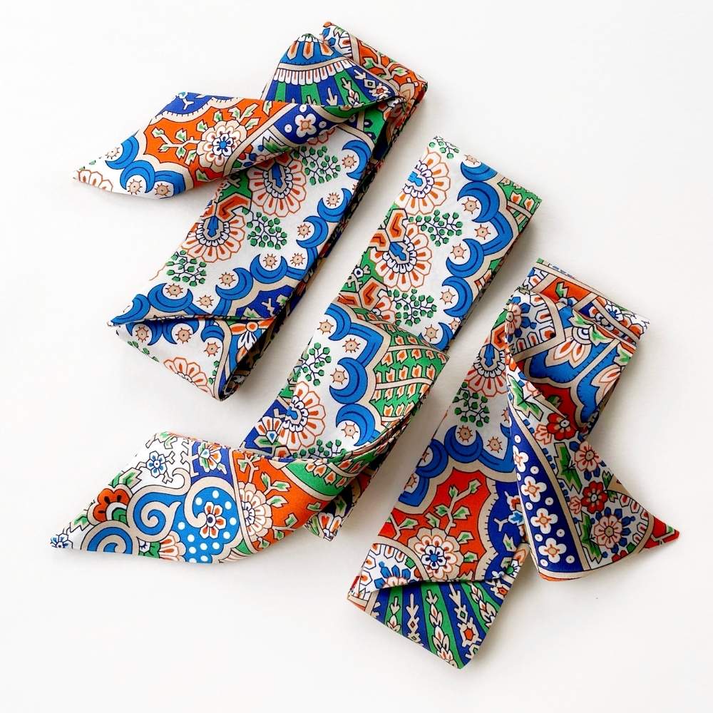 liberty silk skinny neck scarf with traditional japanese motifs in blue, orange, green, and white, arranged on a plain white background.